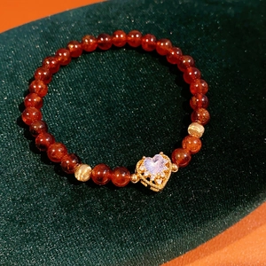 Close-up of red agate beads with golden heart pendant on dark green velvet