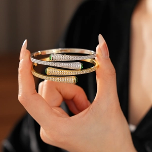 Detail view of gold and silver plated open bangles with green drop stones and micro zircons