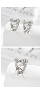 Close-up of silver-tone bear and bow cartilage earrings with cubic zirconia and white pearls