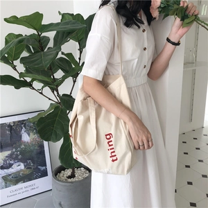 Detail of off-white canvas tote bag featuring red thing letter print in minimalist setting