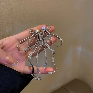 Détail de boucles d'oreilles nœud argenté avec pompons et texture de métal liquide en main