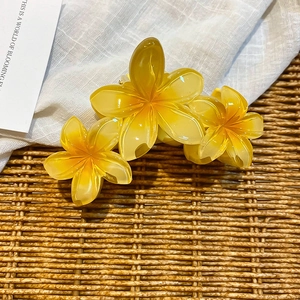 Detail of yellow translucent acrylic frangipani hair claw clip for summer resort styling
