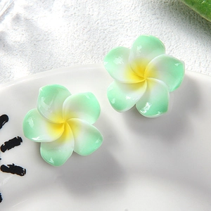 Detail of two resin plumeria flower hair clips with green gradient petals on a white plate