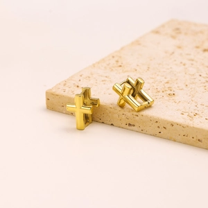 Detail view of golden cross hoop earrings placed on a natural textured stone surface