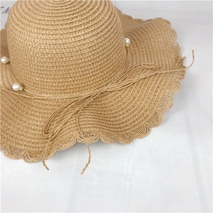 Close-up of a straw sun hat with elegant pearl beads, bow tie and wavy brim edges