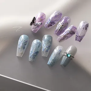 Detail of long coffin nails featuring laser butterfly art, 3D charms, and blue rhinestones