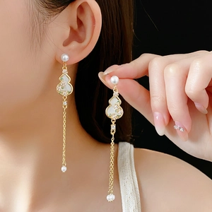 Detail of gold gourd tassel earrings with pearls and green flower patterns on model