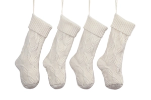 Row of four white cable knit Christmas stockings with hanging loops on white backdrop