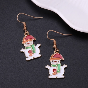 Macro shot of snowman earrings with red hat and green scarf on grey textured surface