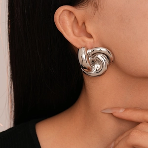 Macro detail of chunky silver knotted stud earrings with a high-polished metallic finish