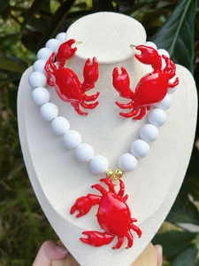 Dettaglio del set collana e orecchini a forma di granchio rosso con perle bianche.