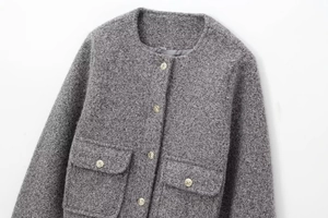 Close-up of grey tweed jacket featuring textured fabric and embossed gold metal buttons