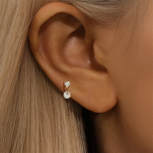Detail of gold heart and round cubic zirconia drop earring worn on the ear