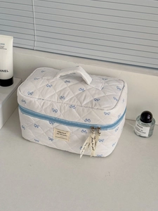 Detail of quilted floral makeup bag with blue bows, top handle and ribbon zipper