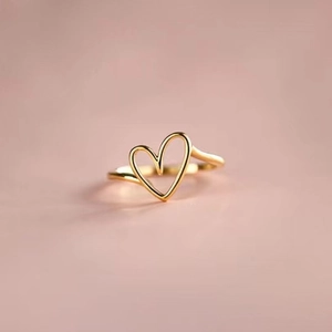 Detail of a minimalist gold heart-shaped ring with a smooth hollow design on pink background