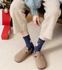 Detail view of navy knit socks with Santa Claus pattern worn with beige suede mule shoes