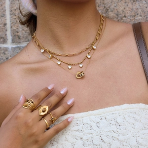 Detalle de collares dorados a capas con colgante de corazón y anillos vintage de ojo de tigre