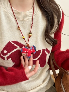 Close-up of ethnic embroidered pony pendant necklace with red hand-woven cotton cord on a model