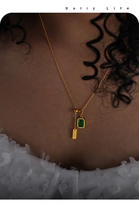 Detail of gold necklace featuring emerald green zircon pendant and BABY tag on model