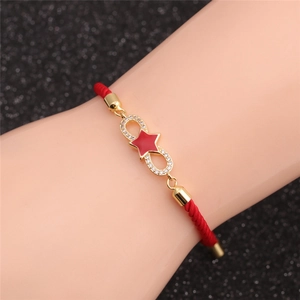 Detail of a red cord bracelet with a gold infinity symbol and sparkling star charm