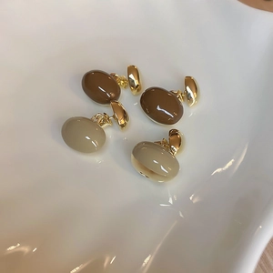 Détail de boucles d'oreilles ovales brillantes en résine caramel et crème dorée