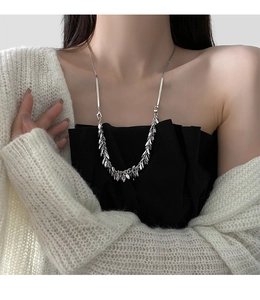 Close-up of a silver wheat-ear sequin necklace on a model wearing a white sweater