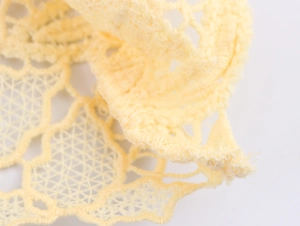 Detailed macro view of delicate light yellow lace fabric with intricate hollow patterns