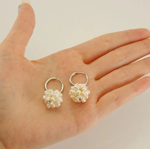 Detail of silver hoop earrings with hand-woven white pearl ball charms shown on palm