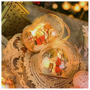 Detail showing two Christmas glass ball ornaments with miniature scenes on a lace tablecloth