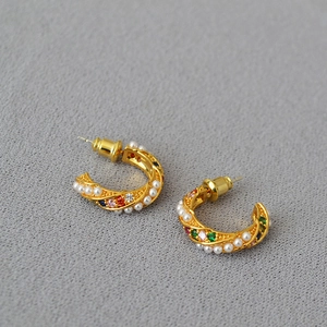Detail of gold C-shape earrings featuring colorful zircons and small white pearls