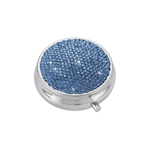 Detailed view of the push-button latch on a round silver pill box with blue rhinestones