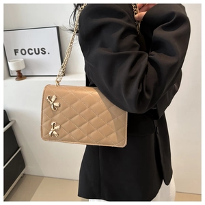 Detail of khaki quilted crossbody bag with golden butterfly accent on a model
