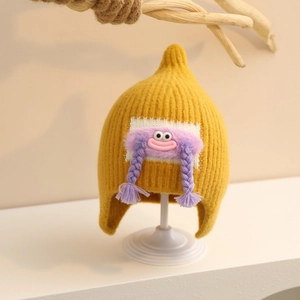 Detail of yellow knit baby hat with earflaps and purple monster patch with braids