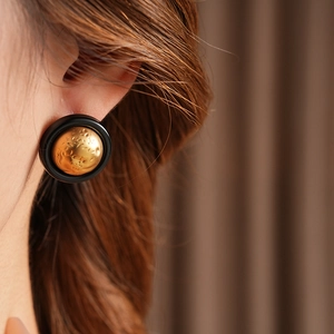 Detailed close-up of retro round earrings with gold hammered texture and black resin frame