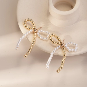 Detail of elegant bow earring featuring gold beads and white pearls on cream ceramic base