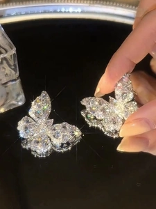 Detailed close-up of butterfly earrings with shimmering zircons held by a hand