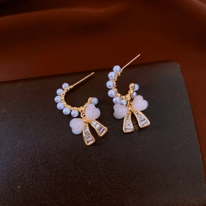 Detail of C-shaped gold earrings with pearls, pink heart charms and bow-shaped zircons