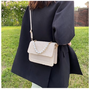 Outdoor shot of beige straw crossbody bag with pearl handle and leather detail