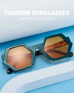 Detail of hexagonal dark green sunglasses with orange lenses on geometric pedestals