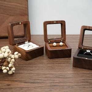 Three walnut wood jewelry boxes with glass lids showing velvet ring cushions on wood table