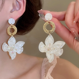 Detailaufnahme weißer Harzblumen-Ohrhänger mit goldfarbenen Ringen in Hammerschlag-Optik