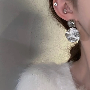 Boucles d'oreilles argentées avec perle carrée et pendentif rond portées par un modèle