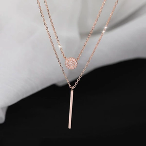 Macro detail of a double-layer rose gold necklace featuring a zircon ball and vertical bar