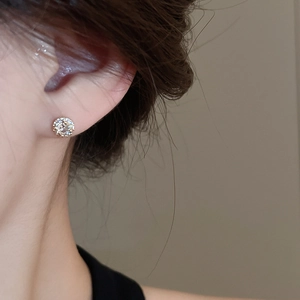Close-up of minimalist gold-plated stud earring with sparkling zircons on model ear