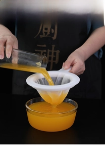Fine mesh kitchen strainer filtering orange juice into a glass with long handle grip
