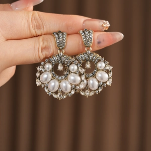 Détail de boucles d'oreilles vintage dorées avec perles et cristaux dans la main