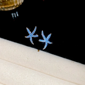 Macro di orecchini a stella marina blu con scintillanti zirconi su sfondo scuro a contrasto