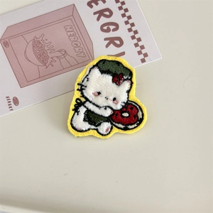 Macro detail of cartoon cat plush embroidery patch with green hat and red donut
