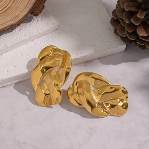 Détail de boucles d'oreilles torsadées dorées sur marbre blanc et décor en bois rustique