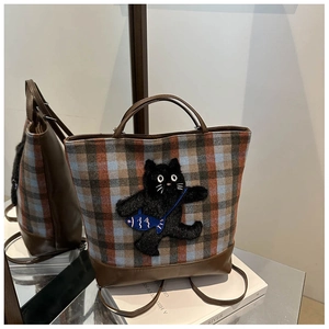 Detail of plaid tote bag featuring a 3D plush black cat patch on a mirror reflection